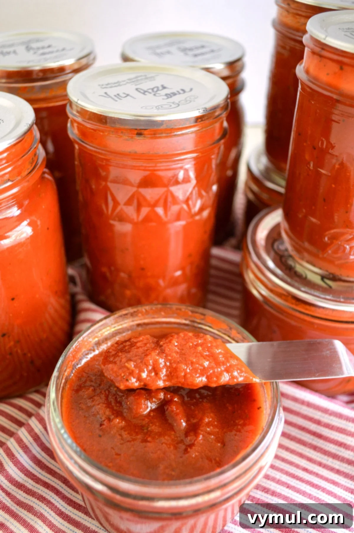 Simple Homemade Pizza Sauce for Canning Fresh or Frozen Tomatoes 2 jars of pizza sauce with one open showing thickness on knife