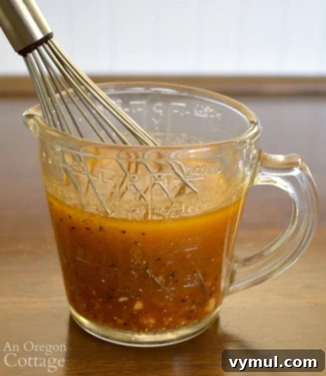 Ingredients for making the Cumin Lime Slaw Vinaigrette being whisked in a glass measuring cup, showcasing fresh lime, garlic, and spices.