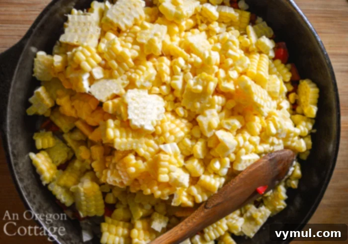 Fresh corn kernels in a pan with sautéed onions and peppers, cooking on the stove.
