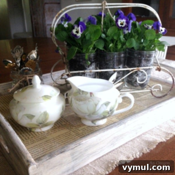 Effortless Live Plant Displays in Mason Jars 4 Close-up of pint mason jars filled with vibrant live pansies, artfully arranged in a vintage glass holder on a decorative tea tray. The centerpiece is completed with elegant spoons and a sugar and creamer set, creating a charming and easy table decoration.