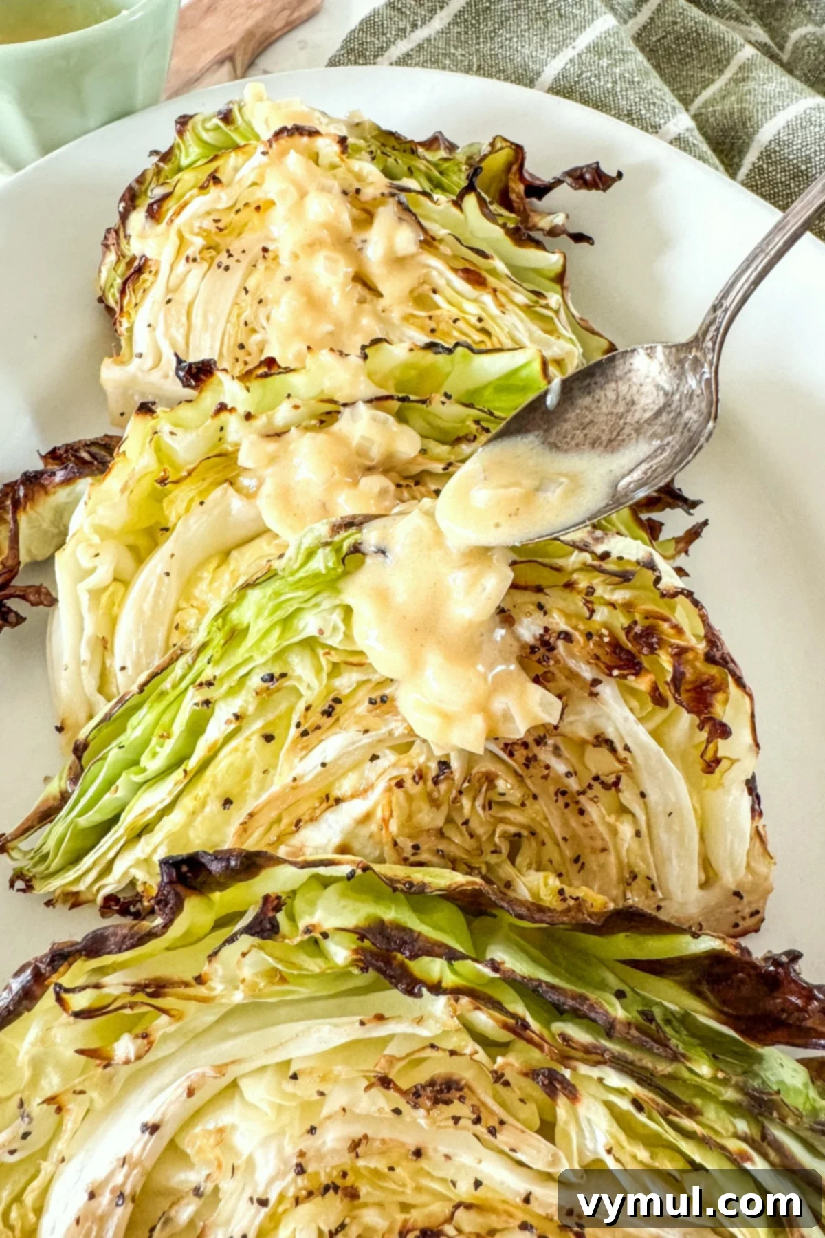 Golden Roasted Cabbage with Zesty Onion Dijon Sauce 8 Roasted cabbage wedges on a platter being drizzled with the onion-Dijon sauce from a spoon.