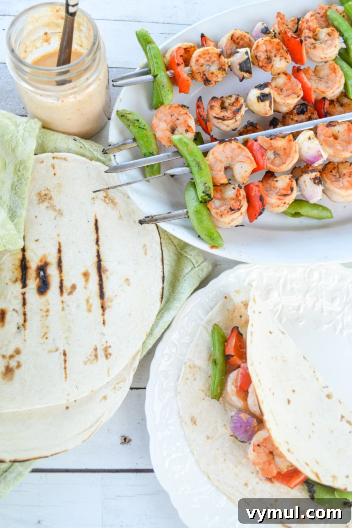 Plates piled high with grilled shrimp tacos, skewers, and warm tortillas, ready to be assembled, viewed from above.