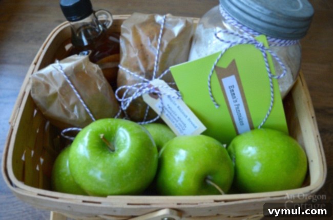 A rustic breakfast gift basket featuring a jar of homemade pancake mix, pure maple syrup, and fresh green apples, tied with twine.