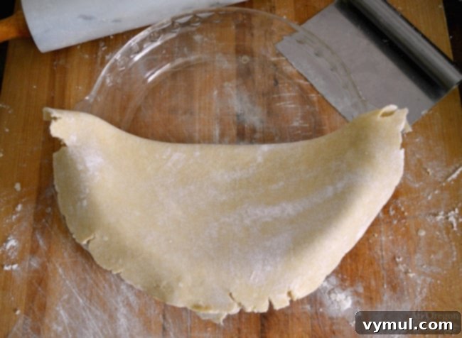 Transferring rolled pie dough to a pie plate by folding it in half for easy placement.