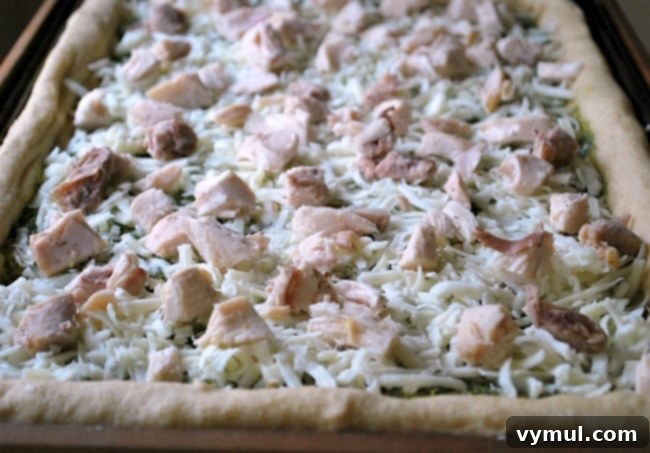 Adding cooked and chopped chicken pieces evenly over the mozzarella cheese layer on a Greek style pizza