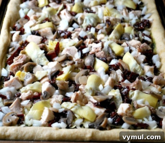 Layering quartered artichoke hearts, mushrooms, onions, dried tomatoes, and Kalamata olives onto the chicken and cheese base of a Greek style pizza