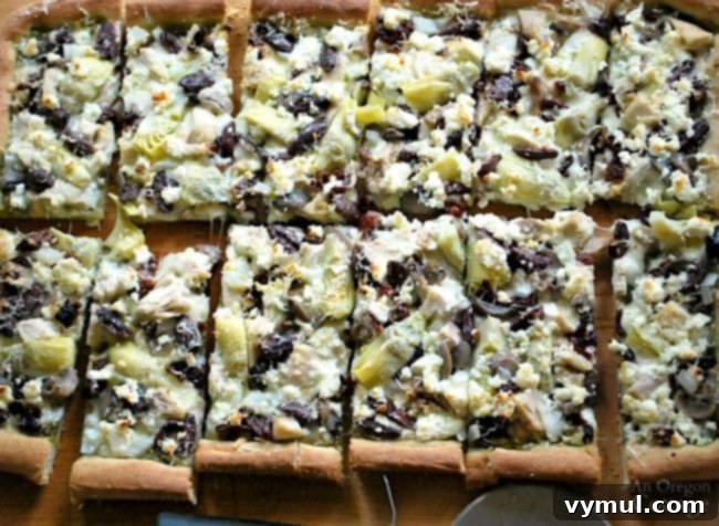 A whole Pesto Chicken Greek Style Pizza, vibrant and freshly baked, on a wooden cutting board