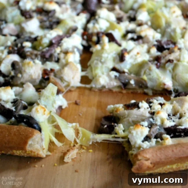 Close-up of a homemade Pesto Chicken Greek Style Pizza slice, showing rich toppings and perfectly baked crust