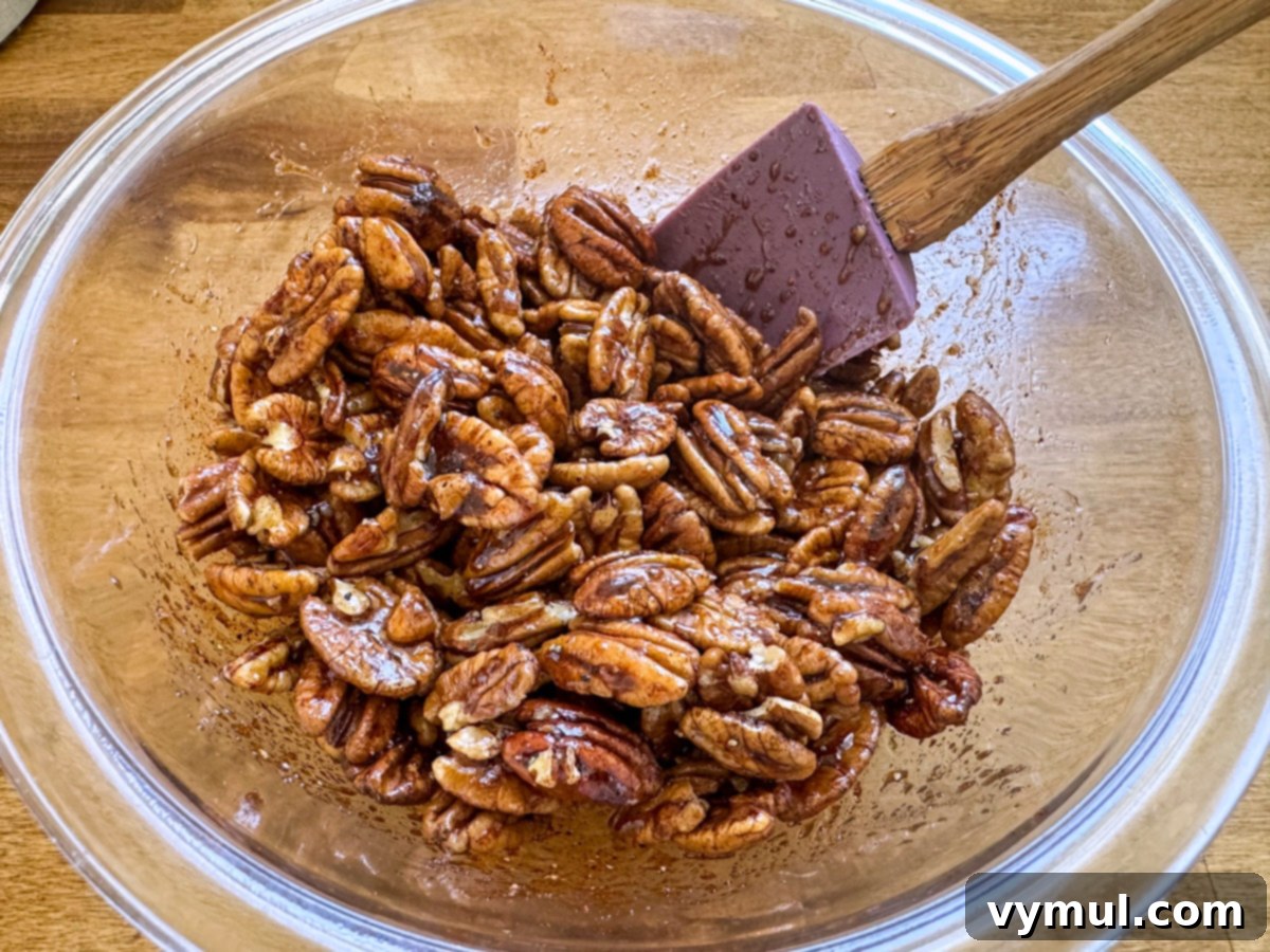 mixing maple syrup, olive oil, and spices with pecan halves in a glass bowl