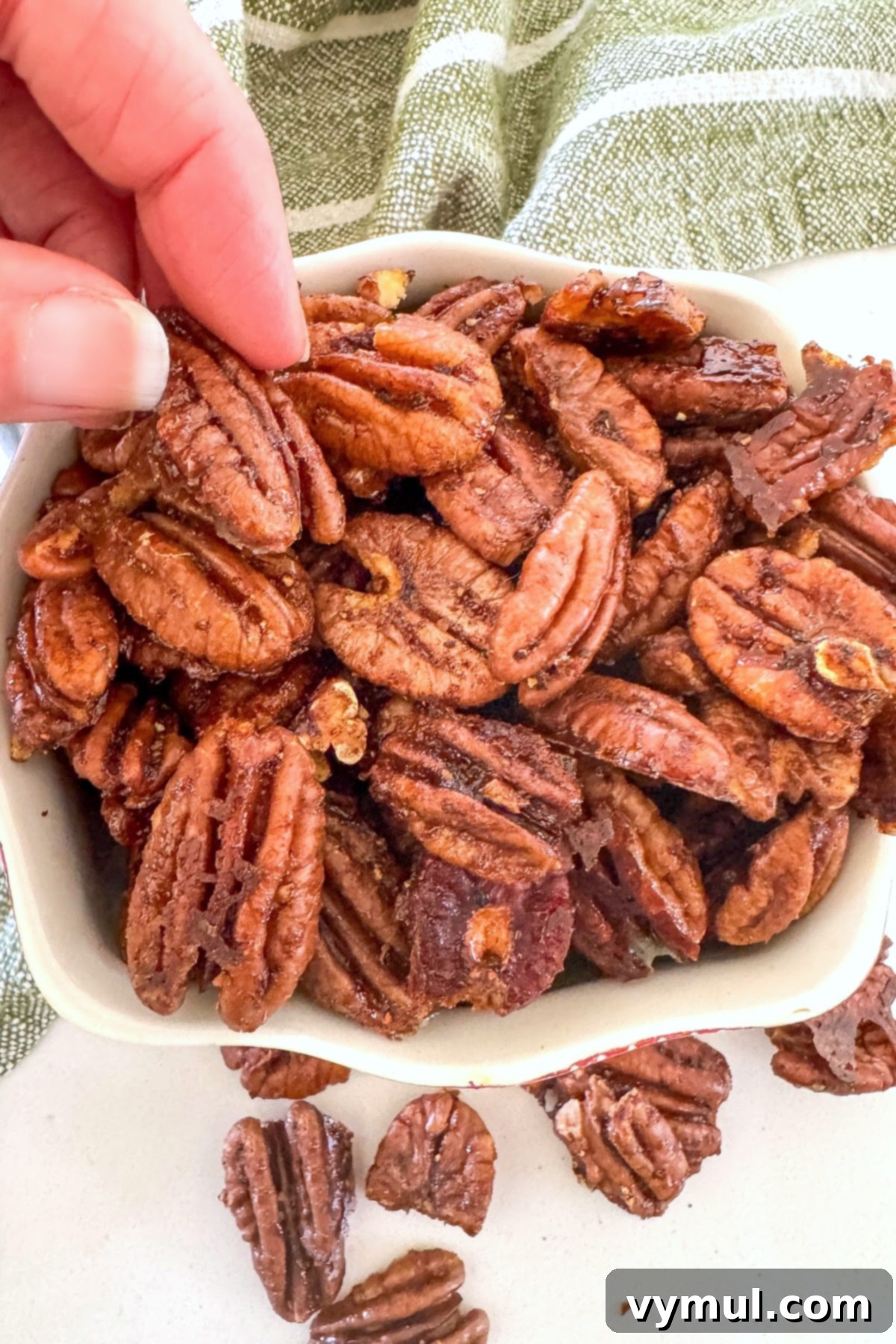 hand grabbing maple candied pecans from a white bowl, ready for snacking