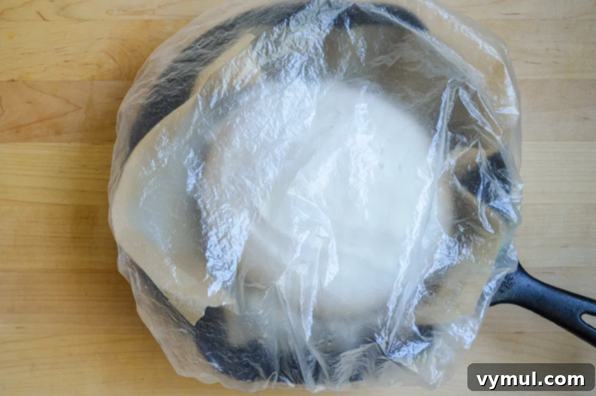 The One-Day Sourdough Secret: Artisan Bread Made Simple 10 final rise of sourdough bread dough in a small skillet with plastic cover, ready for baking