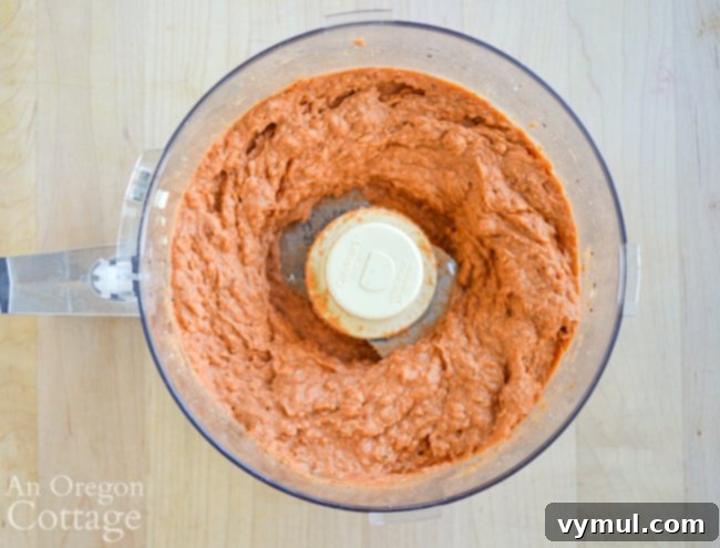 Blended white bean dried tomato dip in a food processor, smooth and reddish.