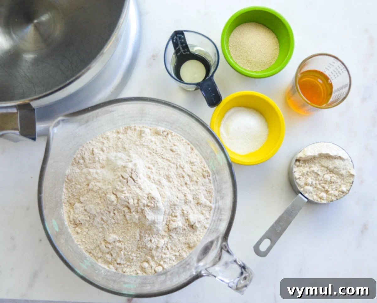 Easy 1-Hour Homemade Pigs In a Blanket 3 Ingredients for pigs in a blanket dough laid out on a marble countertop, including flour, yeast, honey, oil, water, and salt.