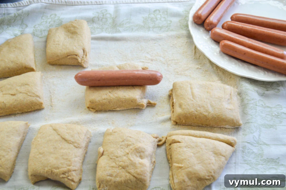 Easy 1-Hour Homemade Pigs In a Blanket 6 Hot dog being placed onto a rectangular piece of homemade dough, ready for wrapping.