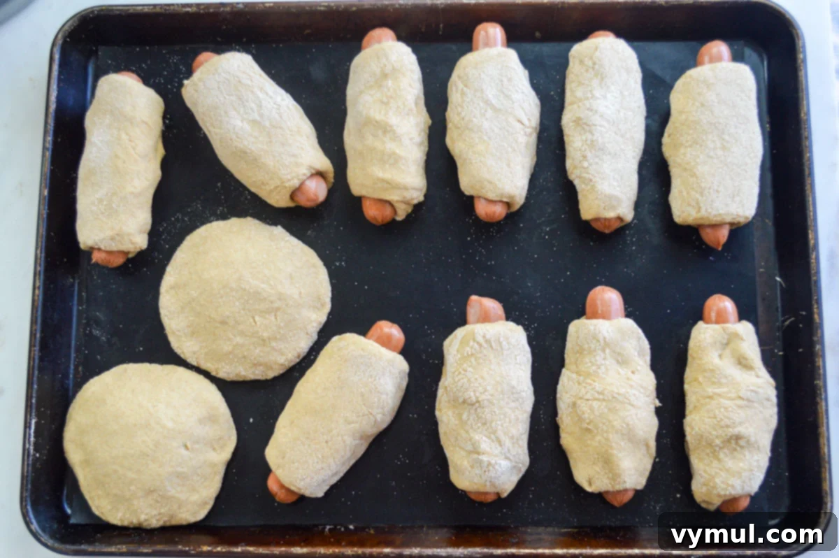 Easy 1-Hour Homemade Pigs In a Blanket 8 Neatly wrapped hot dogs on a baking sheet, seam-side down, ready to be baked into pigs in a blanket.