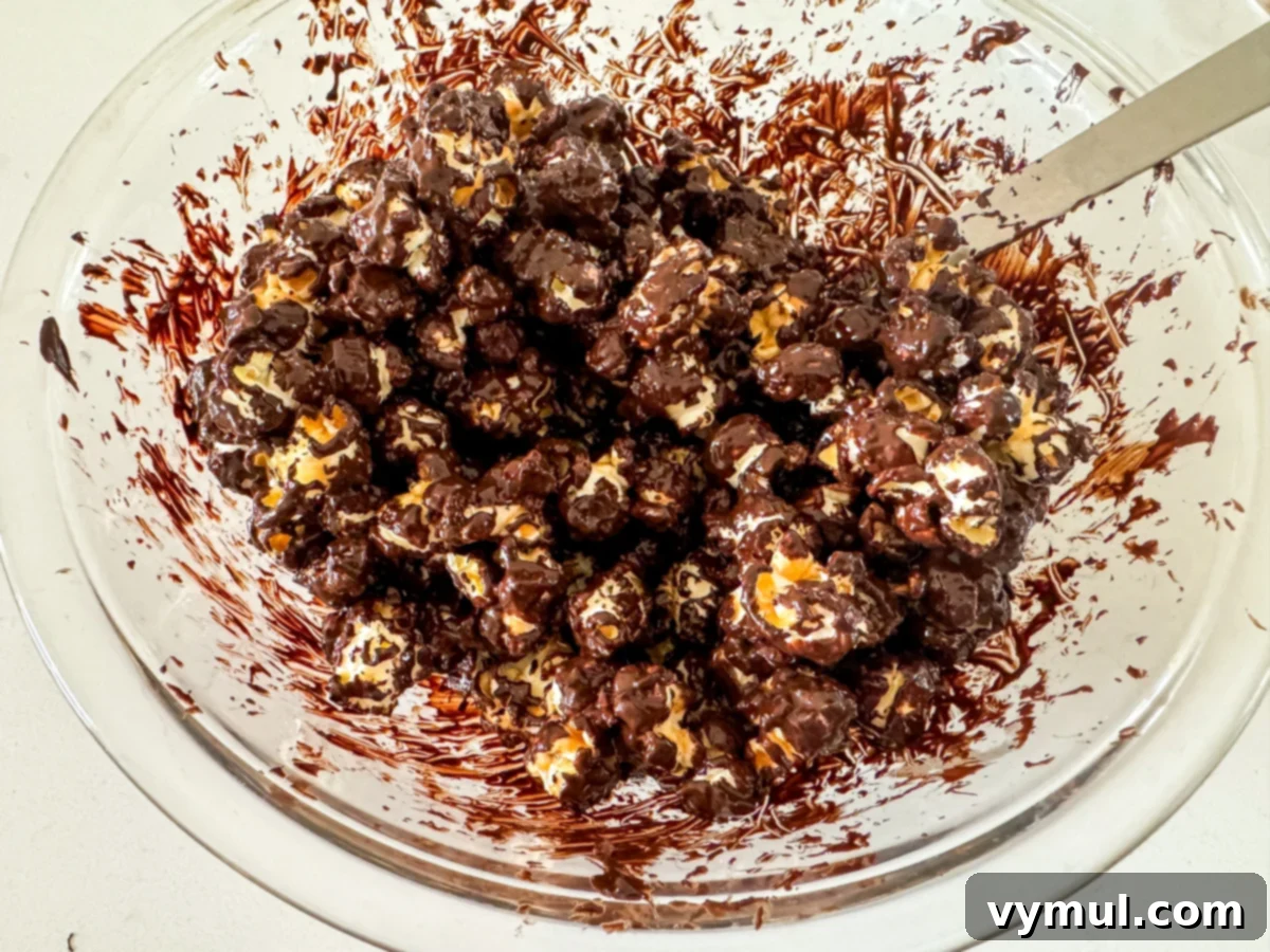 Foolproof Moose Munch Caramel Corn No Corn Syrup No Thermometer 11 Caramel corn being thoroughly coated in melted chocolate within a large mixing bowl.