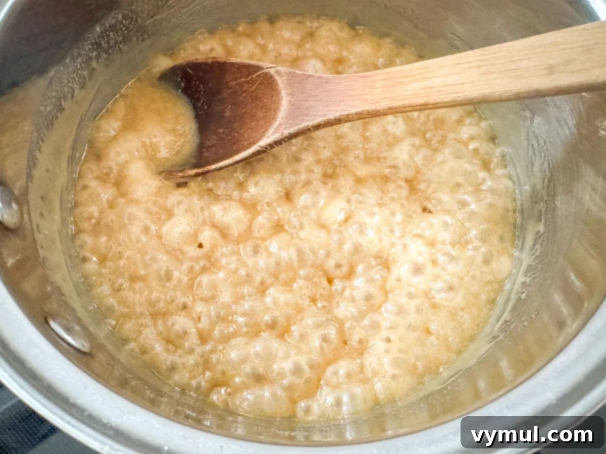 Foolproof Moose Munch Caramel Corn No Corn Syrup No Thermometer 7 Caramel sauce gently boiling with a wooden spoon, indicating the 5-minute cooking time has begun.