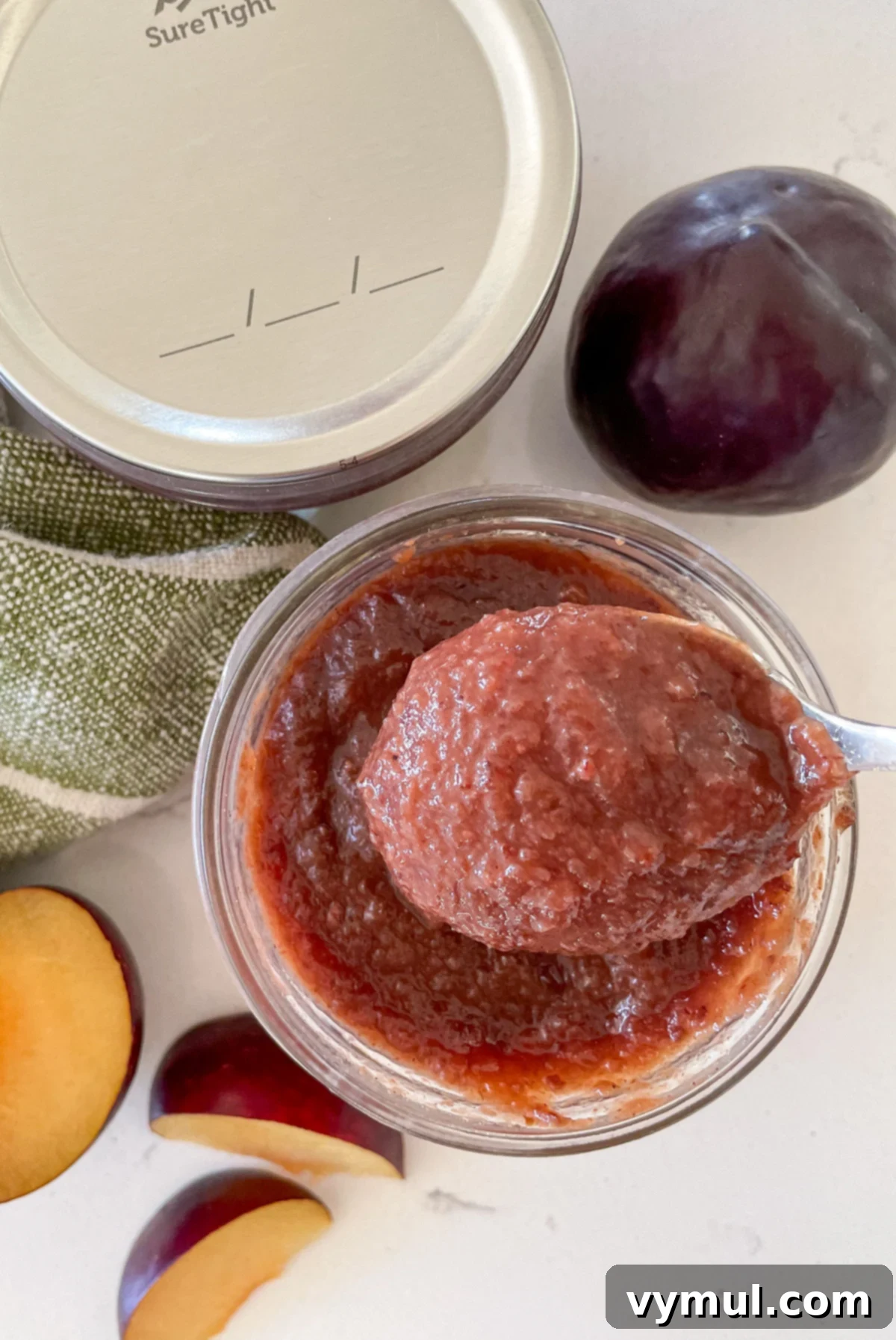 A spoon lifting a serving of homemade plum sauce from a jar, highlighting its rich texture
