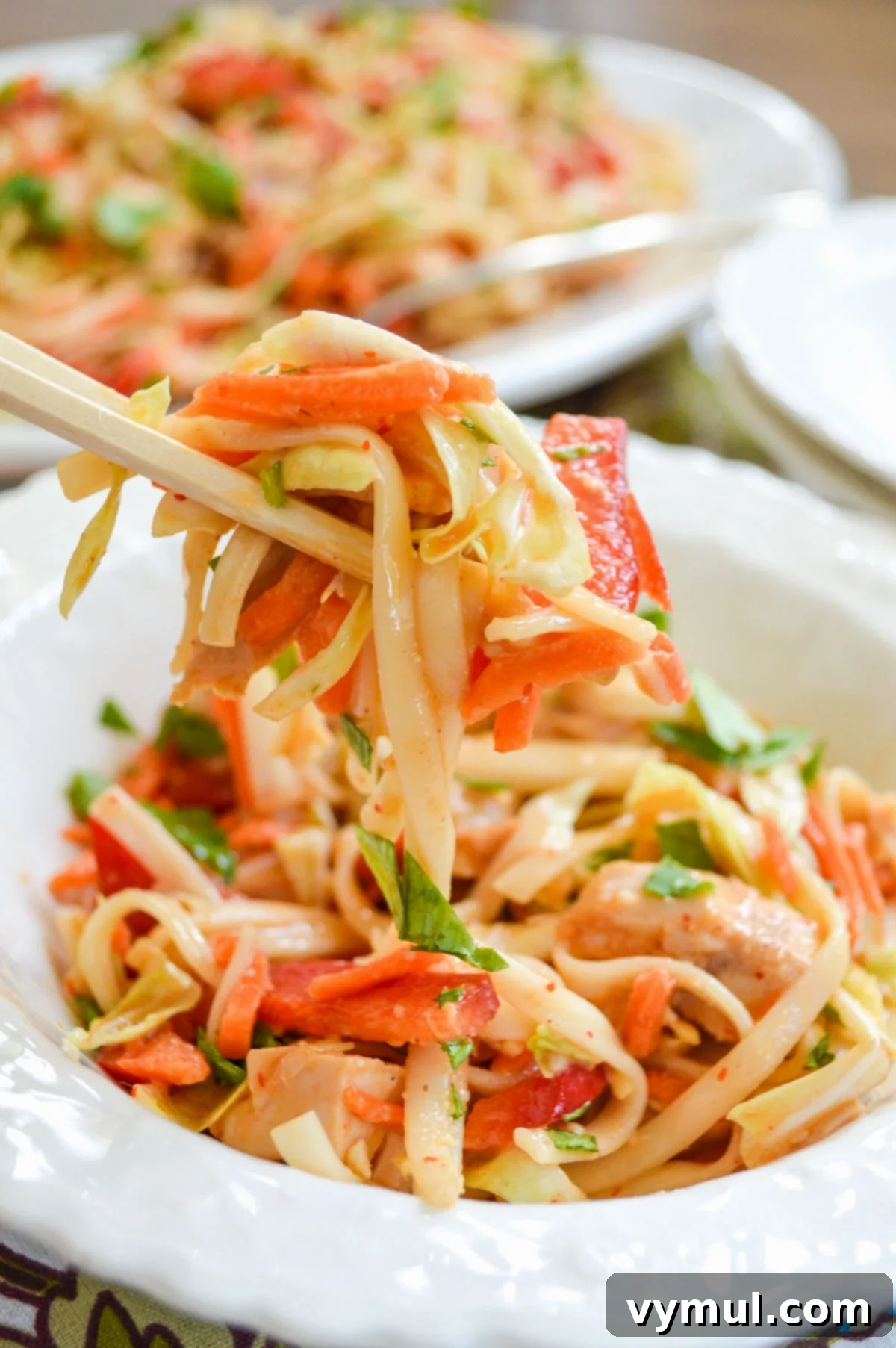 Serving spicy peanut noodles with chicken and chopsticks from a large bowl, garnished with fresh herbs.