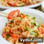 A bowl of flavorful peanut noodles with chicken, ready to eat with chopsticks, showcasing the vibrant colors and creamy sauce.