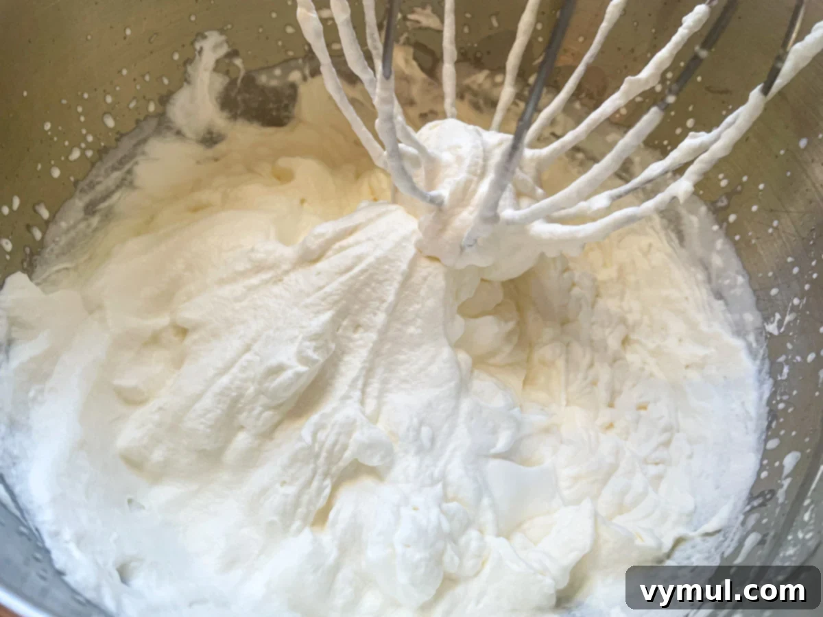 Heavy whipping cream expertly whipped to stiff peaks in a large mixing bowl.