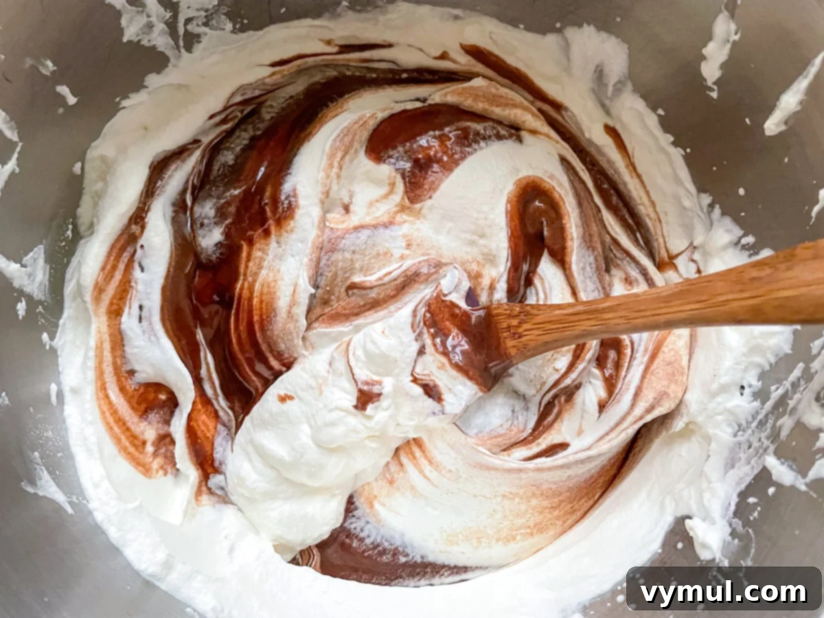 The chocolate-milk mixture being folded into the rest of the whipped cream with a spatula.