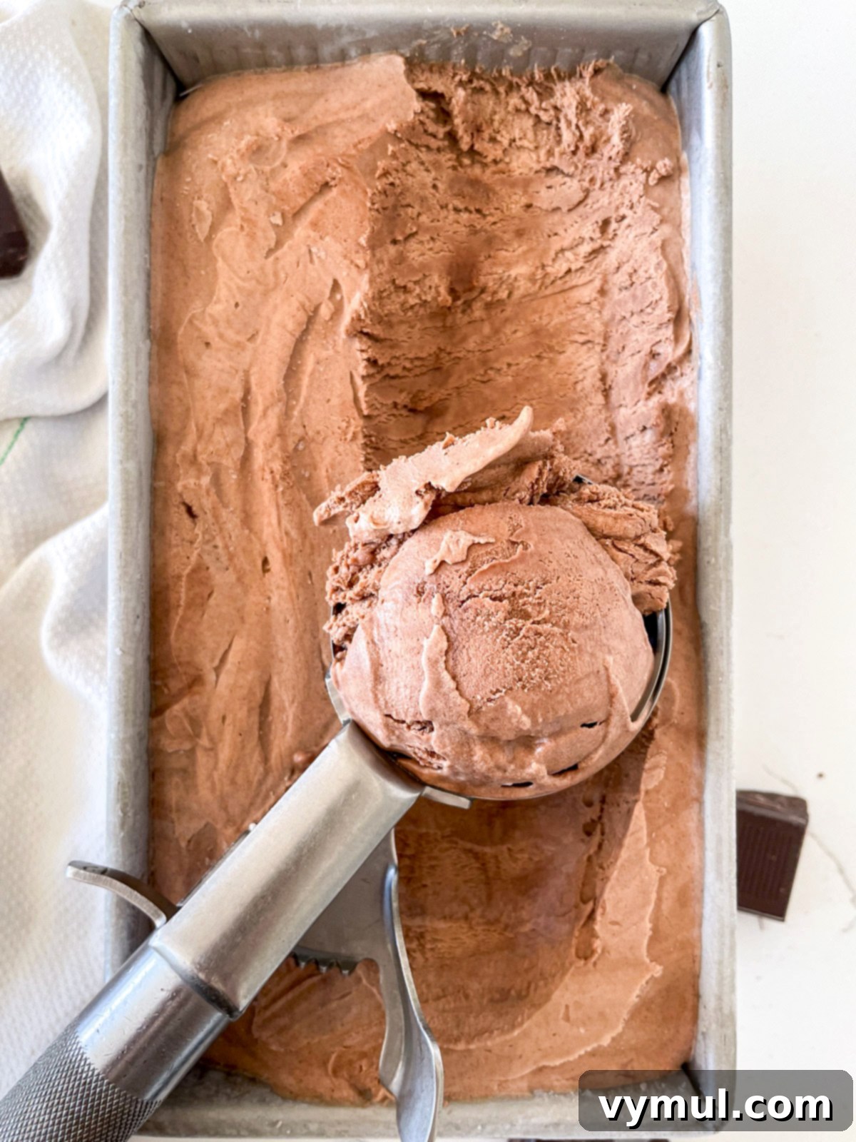 A scoop digging into perfectly frozen no-churn chocolate ice cream in a loaf pan.