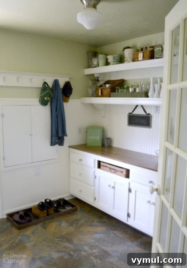 Cottage farmhouse mudroom with painted cabinets, shelves for storage, and practical flooring.