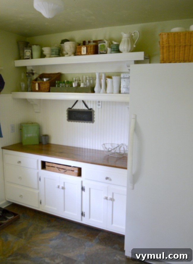 Transformed cottage farmhouse mudroom area with dark, functional flooring, ample storage for gardening supplies, and a freezer.