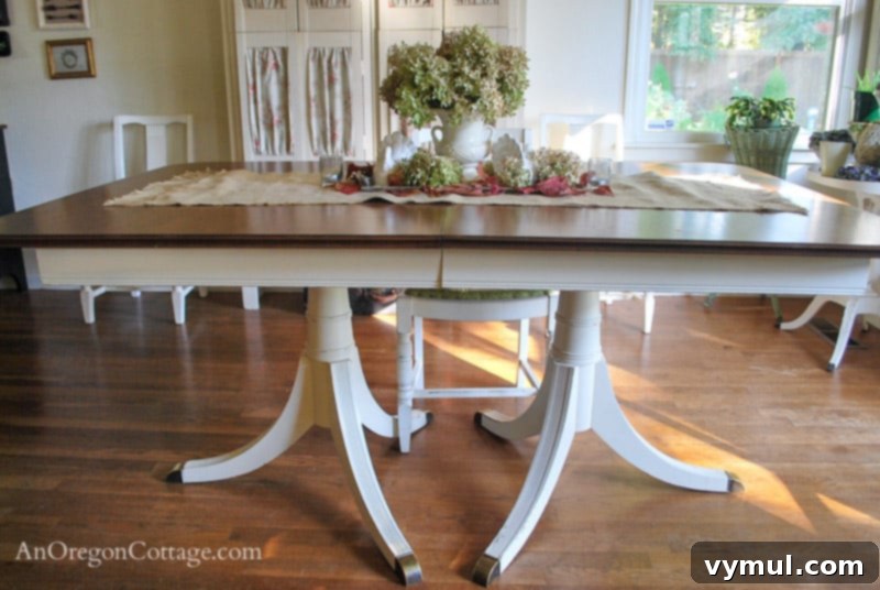 dining table after from side: A elegant dining table after its DIY makeover, featuring a dark wood top and a distressed creamy white base, viewed from the side.