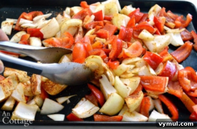 Sheet Pan Sausage & Veggies 4 Hands mixing chopped peppers and onions with olive oil and spices on a baking sheet