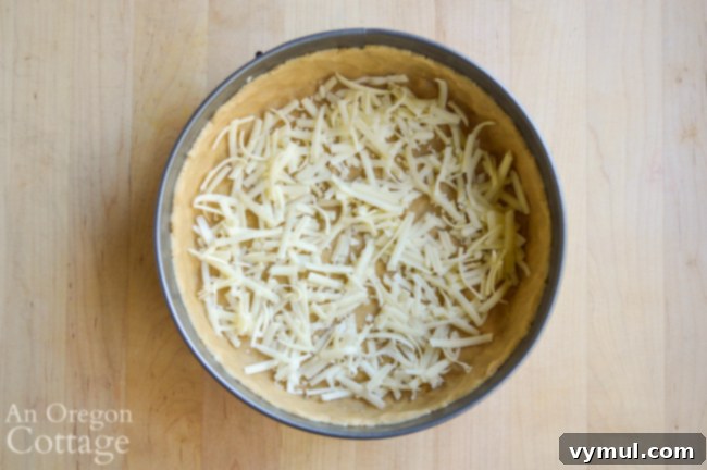 Adding a layer of shredded cheese to the bottom of the chilled quiche crust.