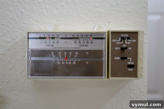 Old, traditional thermostat installed on a wall before a modern Wi-Fi smart thermostat upgrade