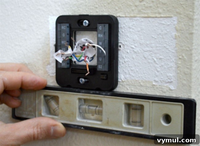 Using a small level to ensure the new thermostat backplate is perfectly straight before final tightening