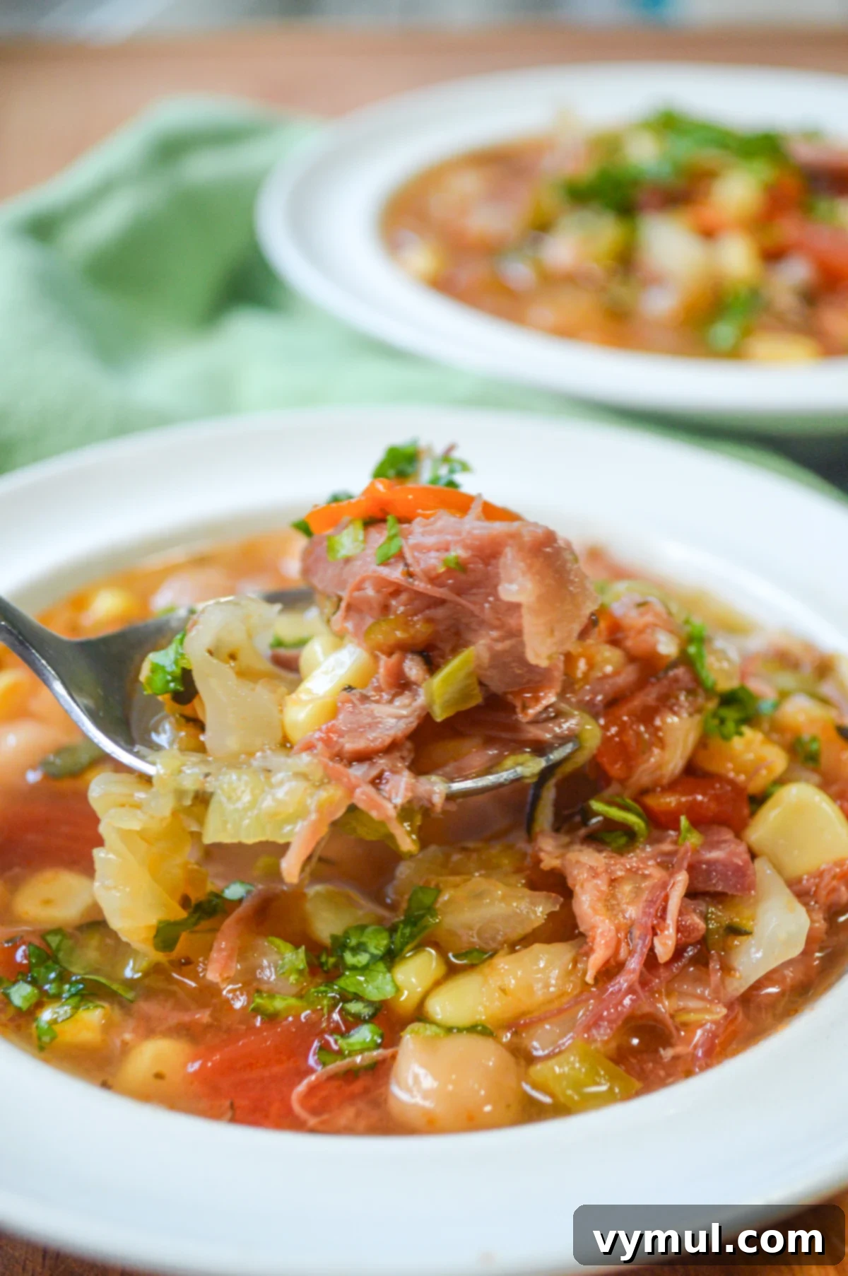 Easy Ham Bone Soup with Beans and Vegetables: Crockpot, Instant Pot, or Stovetop 2 A hearty bowl of homemade ham bone soup with an abundance of vegetables, served on a rustic spoon, showcasing the rich broth and tender ham pieces.