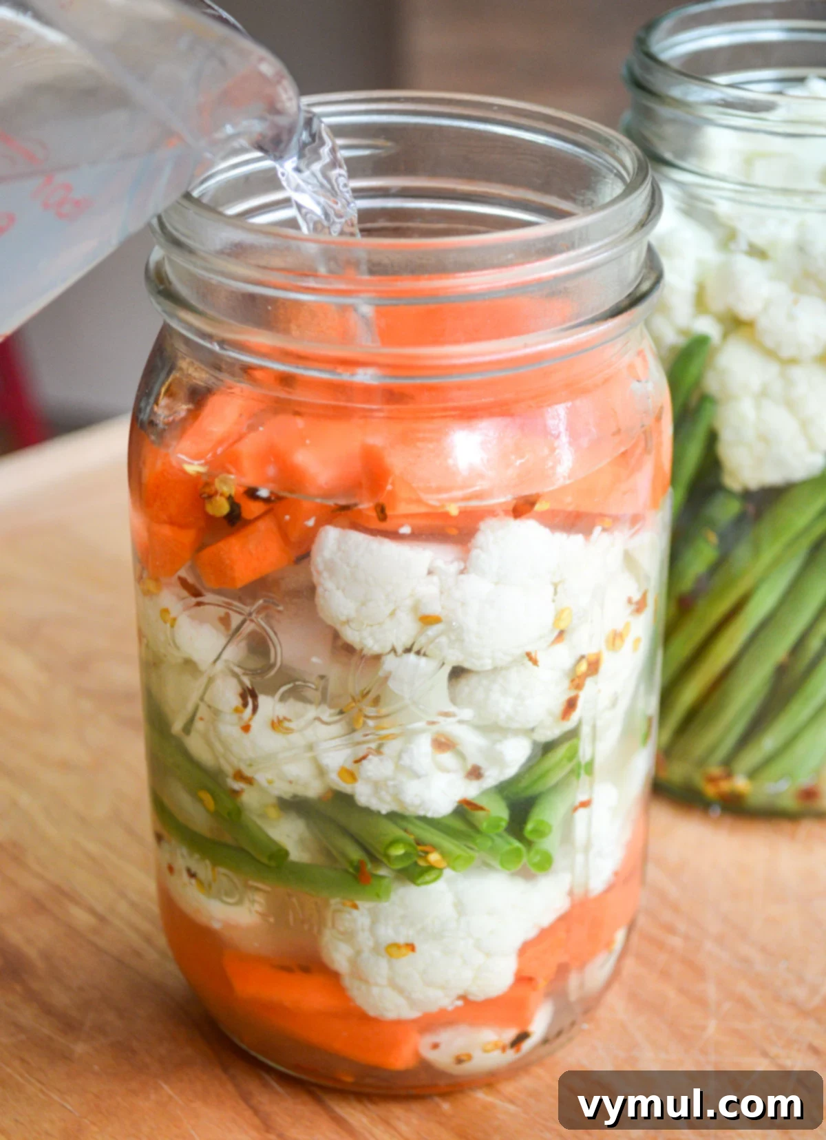 pouring brine into jar of cut vegetables