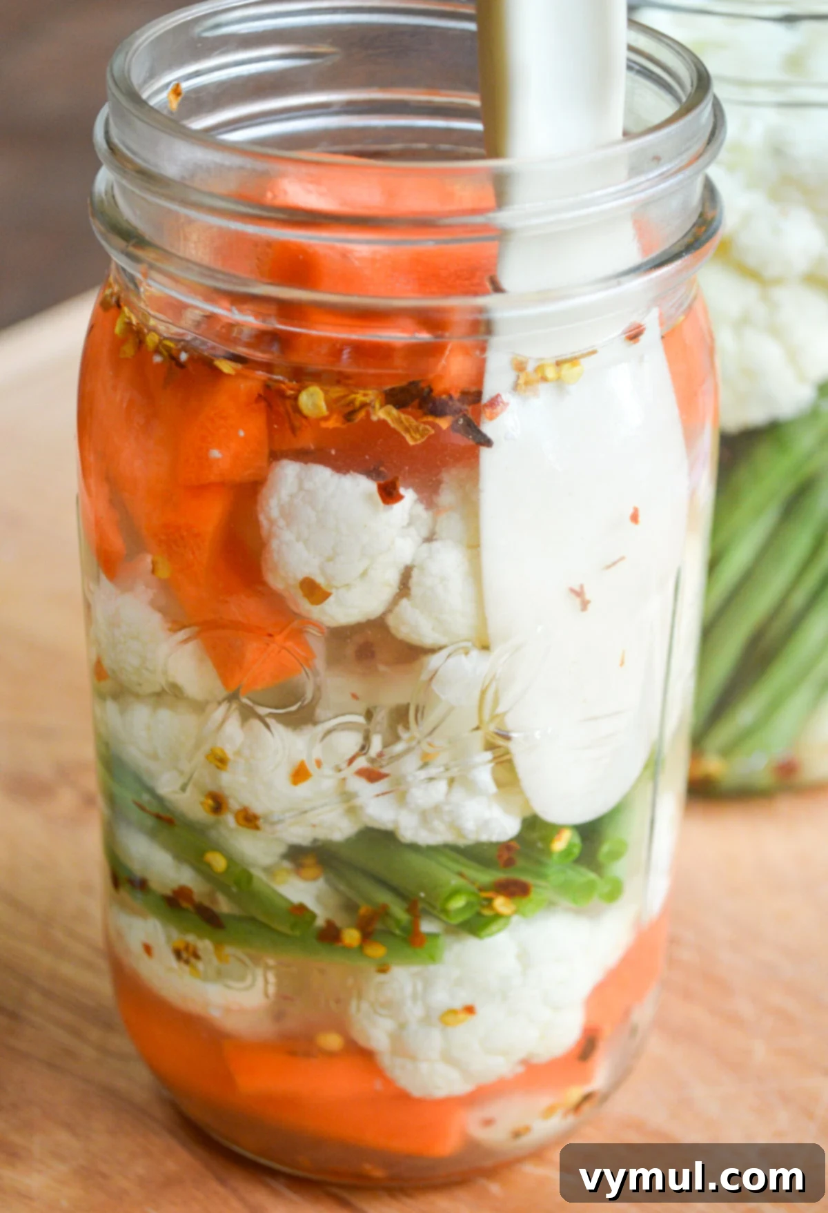 using a spatula to remove air bubbles from jar of vegetables with brine