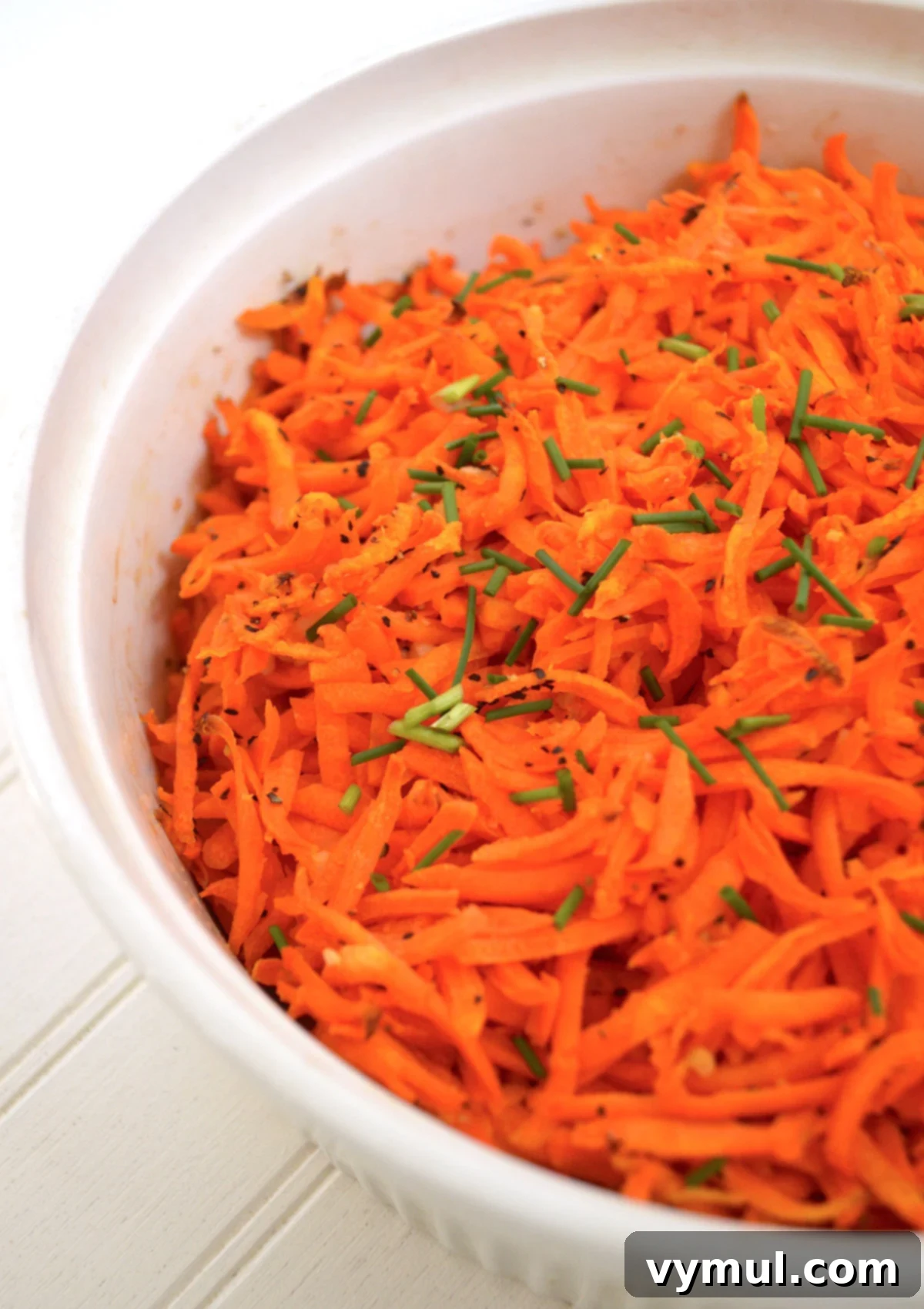 Tangy Lemon Garlic Baked Grated Carrots 2 Close-up of golden brown lemon garlic baked grated carrots in a white serving bowl, garnished with fresh herbs.