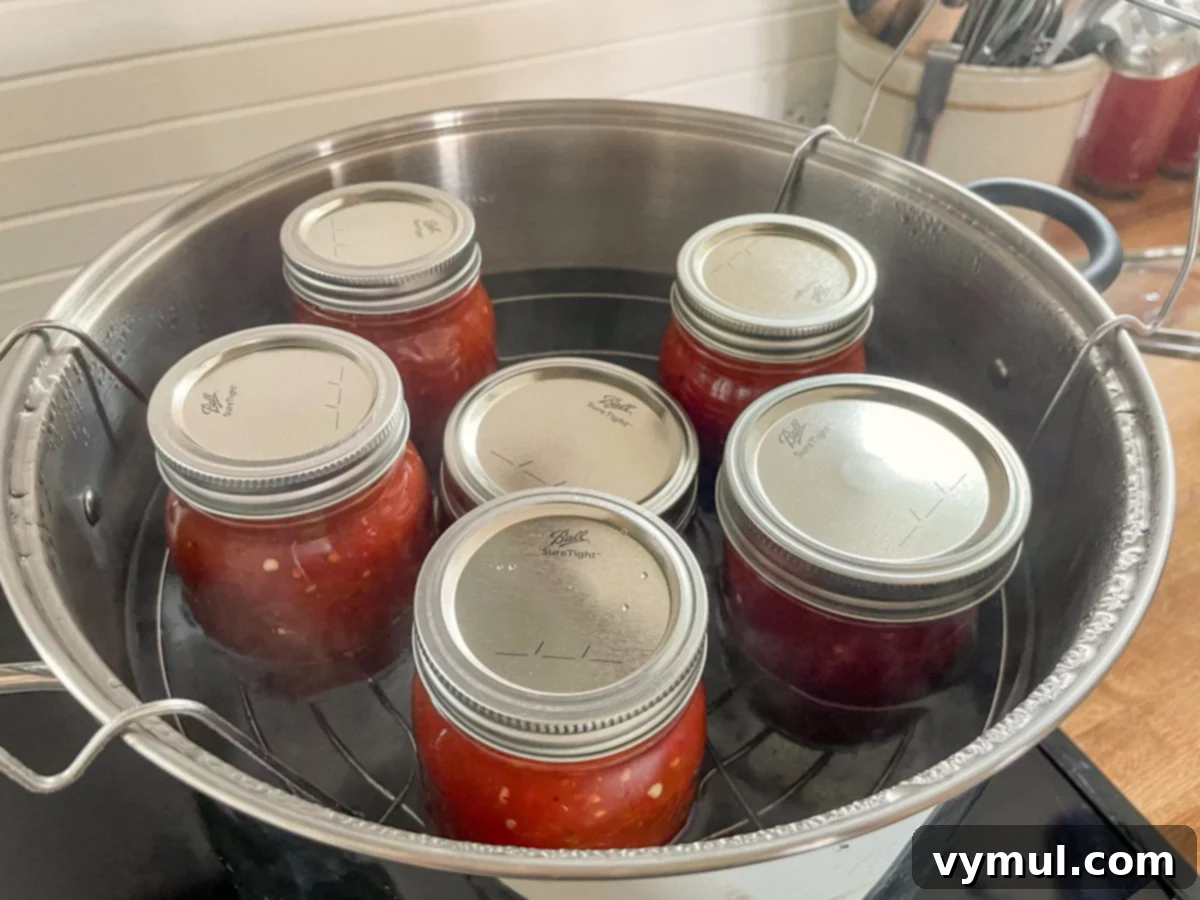 Pint jars of freshly filled homemade salsa being carefully placed into a boiling water bath canner.