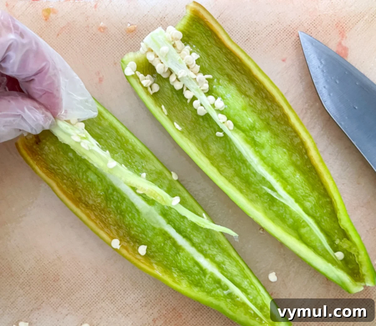 A gloved hand carefully removing seeds from a hot pepper, emphasizing safety when handling spicy ingredients.