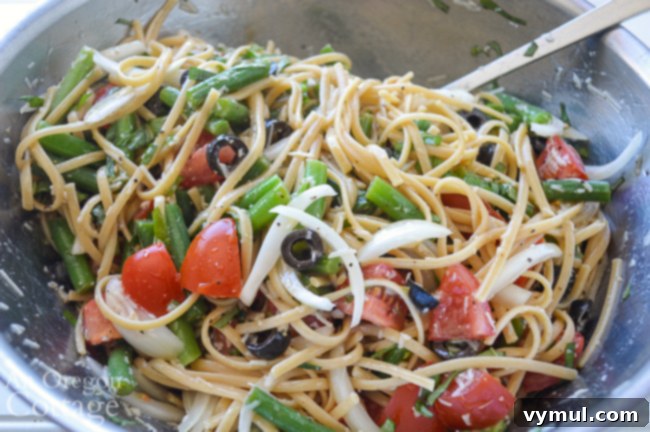Tossing the summer pasta salad ingredients with dressing in a large bowl