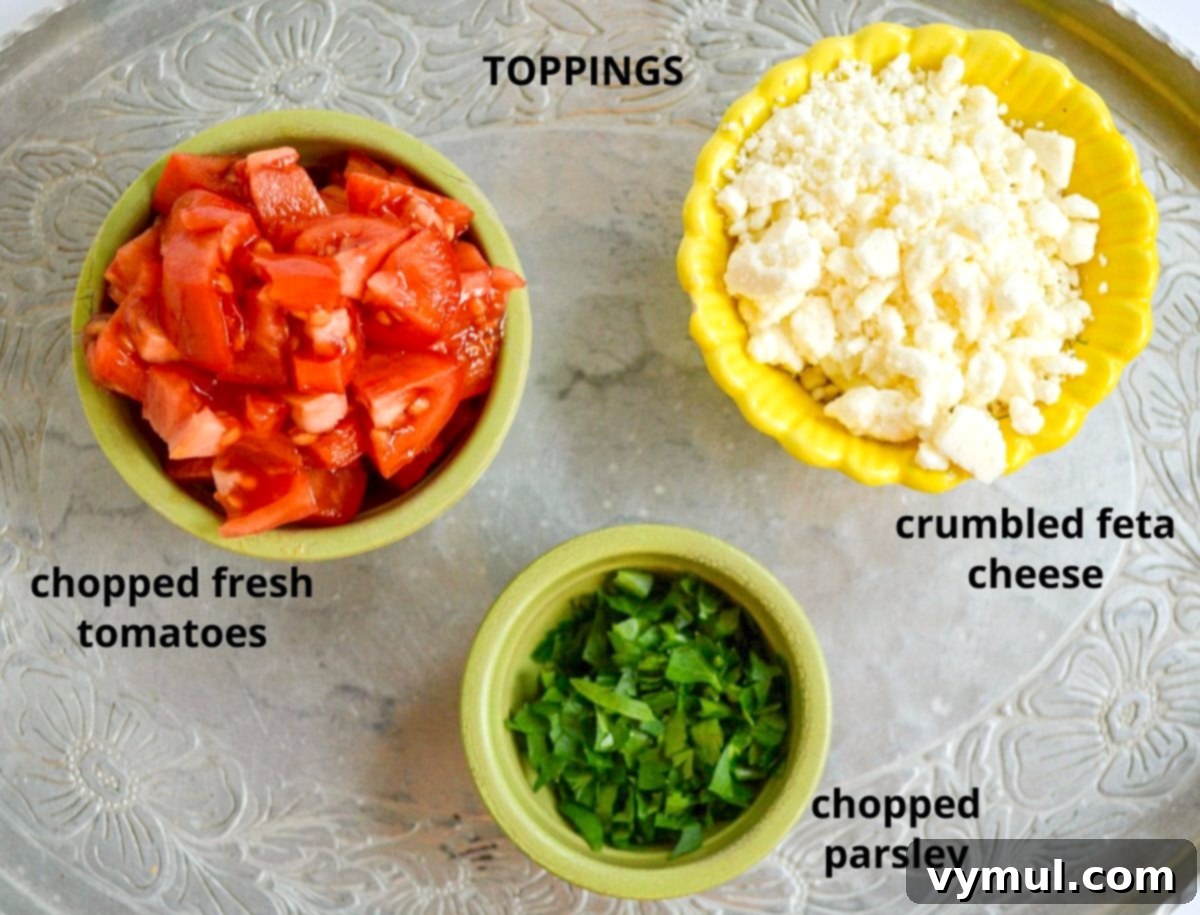 Various Mediterranean toppings for shrimp orzo, including fresh tomatoes, parsley, feta cheese, and Kalamata olives, arranged on a silver tray.