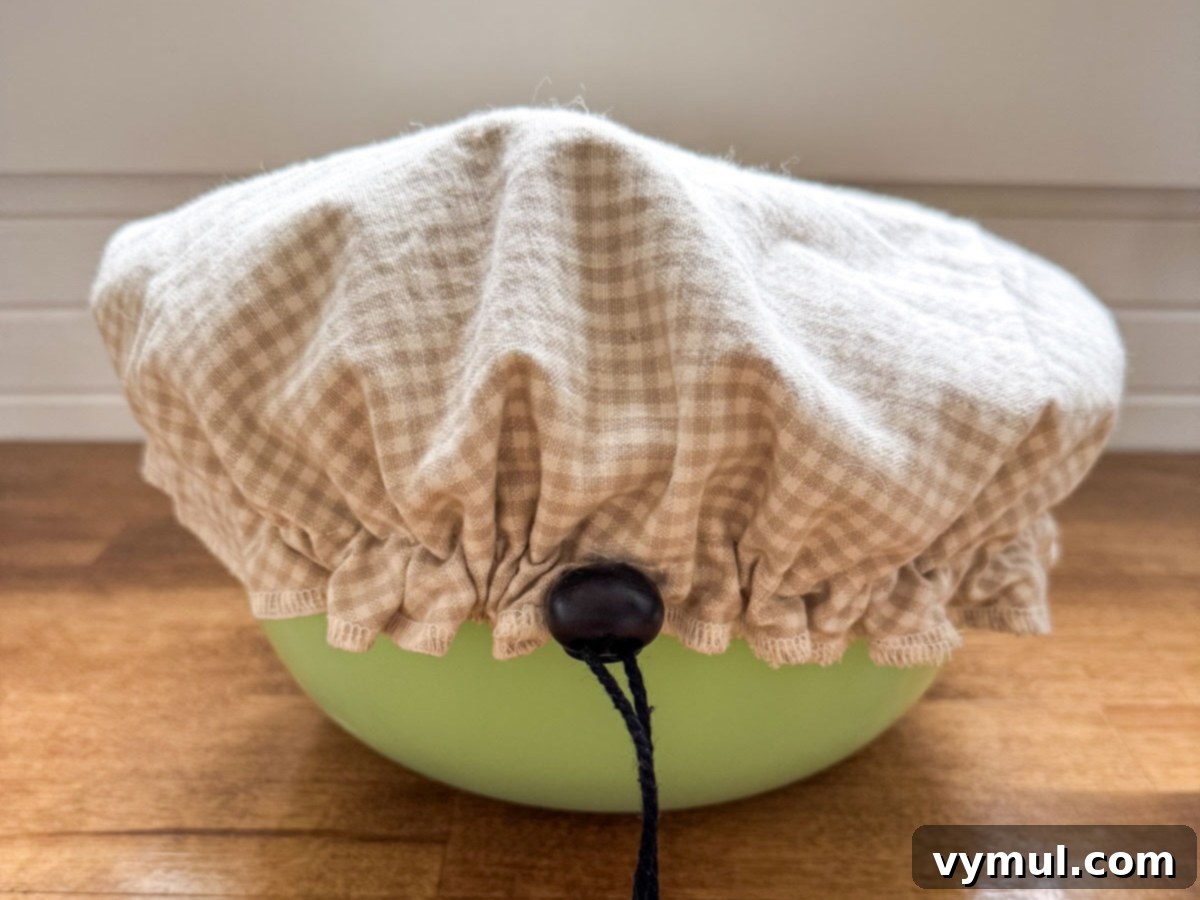 Foolproof Dutch Oven Whole Wheat Artisan Bread 10 Step 3: Green bowl with a fabric bowl cover, indicating proper dough covering for rising.