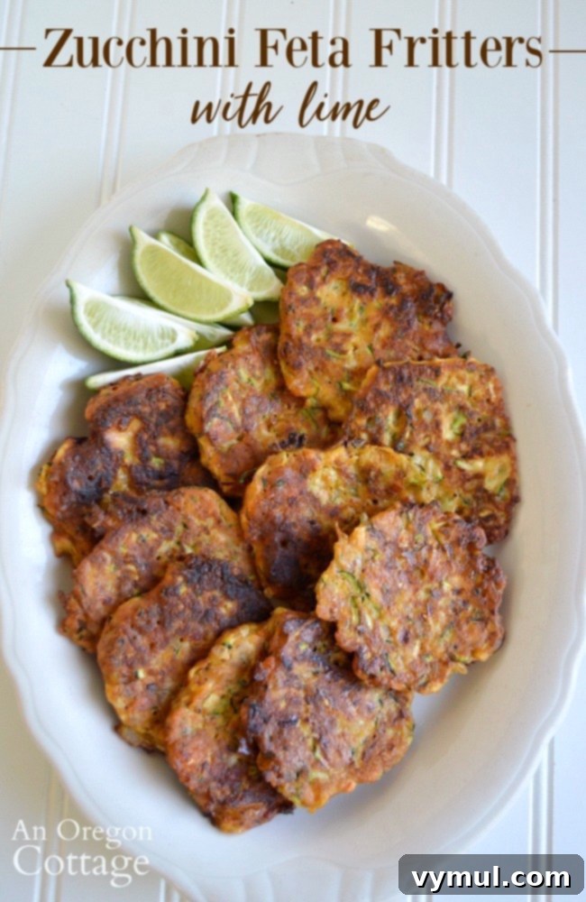 Zesty Zucchini Feta Fritters 12 A large platter filled with golden-brown zucchini feta fritters, garnished with fresh lime wedges, presented as a delicious and versatile dish.