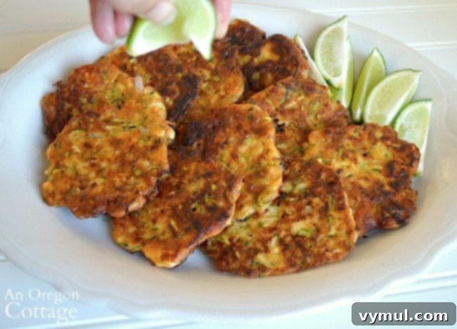 Zesty Zucchini Feta Fritters 3 A hand squeezing fresh lime juice over a stack of golden-brown zucchini feta fritters on a clean white plate, emphasizing the crucial finishing touch.