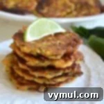 Zesty Zucchini Feta Fritters 10 Freshly cooked zucchini feta fritters stacked on a white plate with lime wedges