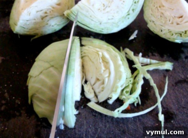 Hands carefully cutting a head of fresh cabbage on a wooden board, preparing it for preserving or cooking.