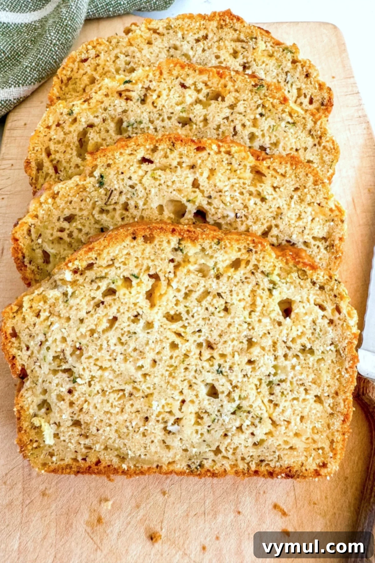 Slices of savory zucchini bread with visible cheese and herbs on a wooden cutting board, ready to be served or eaten as a snack.