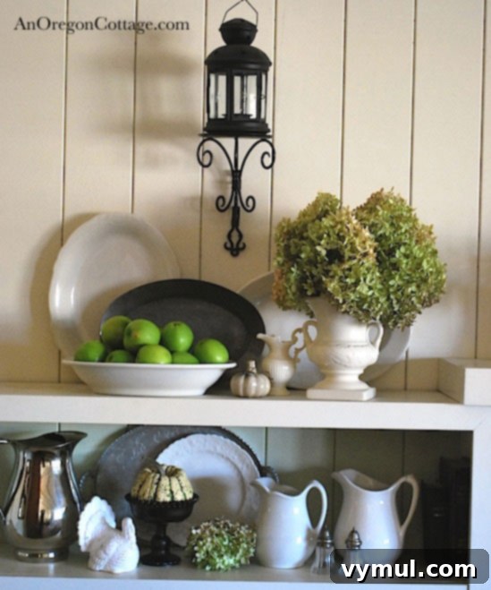 Styled Shelf with Thrift Finds A beautifully styled shelf featuring thrifted white pitchers, vintage pewter, green apples, and a dark glass bowl.