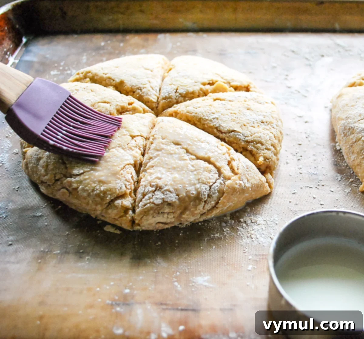 Luscious Double Apple Scones with Golden Caramel Glaze 5 A hand gently brushing the top of scored scone dough with milk, preparing it for baking and optional sugar-cinnamon topping.